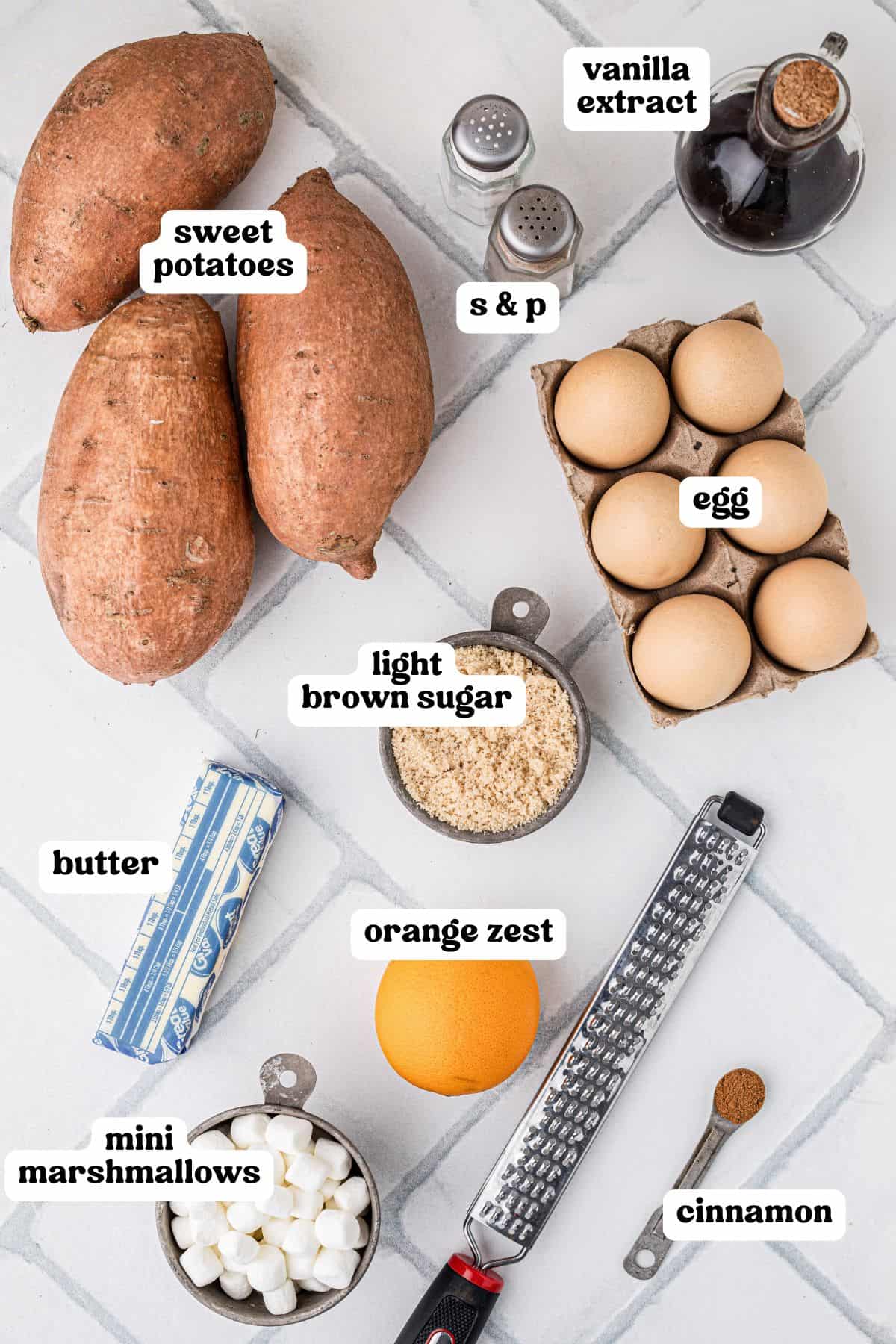 Overhead view of ingredients for sweet potato casserole with text labels, including: sweet potatoes, eggs, vanilla extract, salt and pepper, butter, light brown sugar, orange zest, cinnamon, and mini marshmallows.