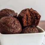 Close-up of several chocolate brownie bites in a white bowl, one brownie bite has a bite taken out of it.