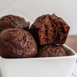 Close-up of several chocolate brownie bites in a white bowl, one brownie bite has a bite taken out of it.
