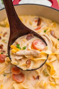 Wooden ladle lifting creamy crack chicken noodle soup from pot.
