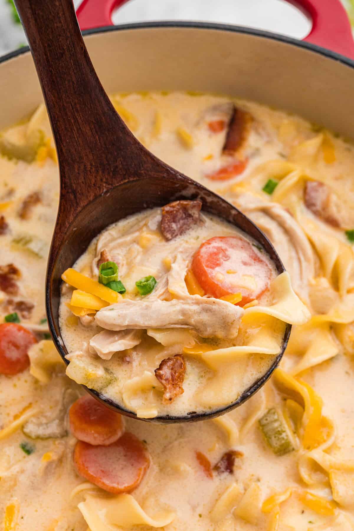 Wooden ladle lifting creamy crack chicken noodle soup from pot.