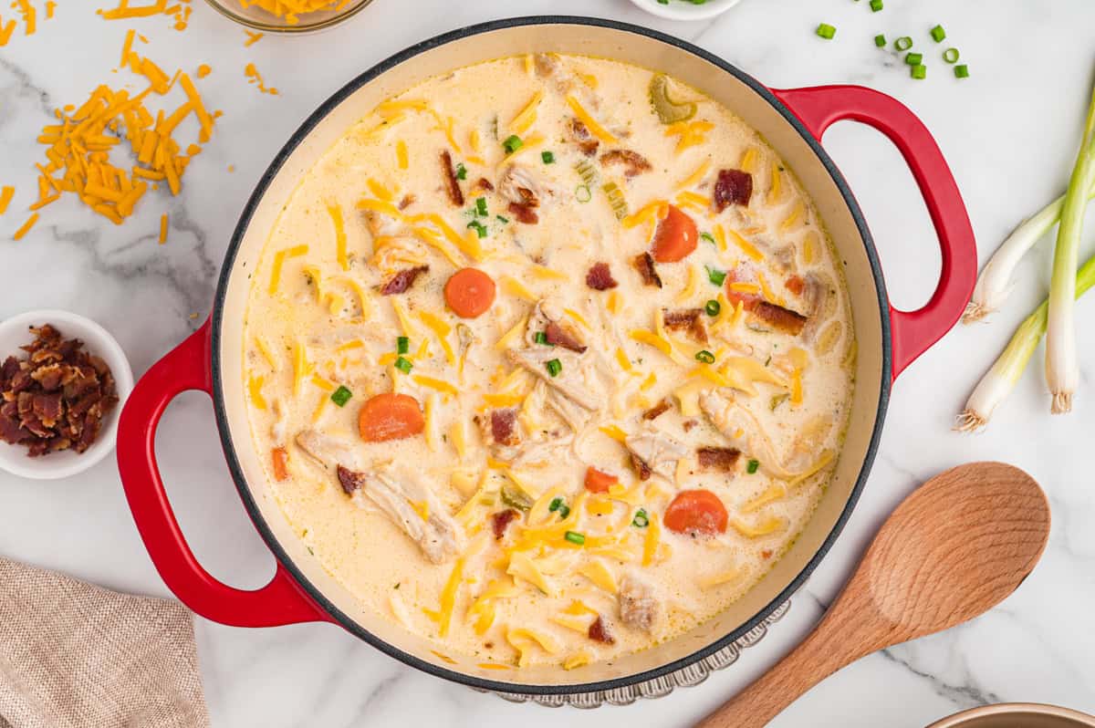 Top-down view of crack chicken noodle soup with egg noodles, bacon and cheese in a red pot.