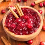 Homemade cranberry sauce in a wooden bowl with whole cranberries cinnamon sticks.