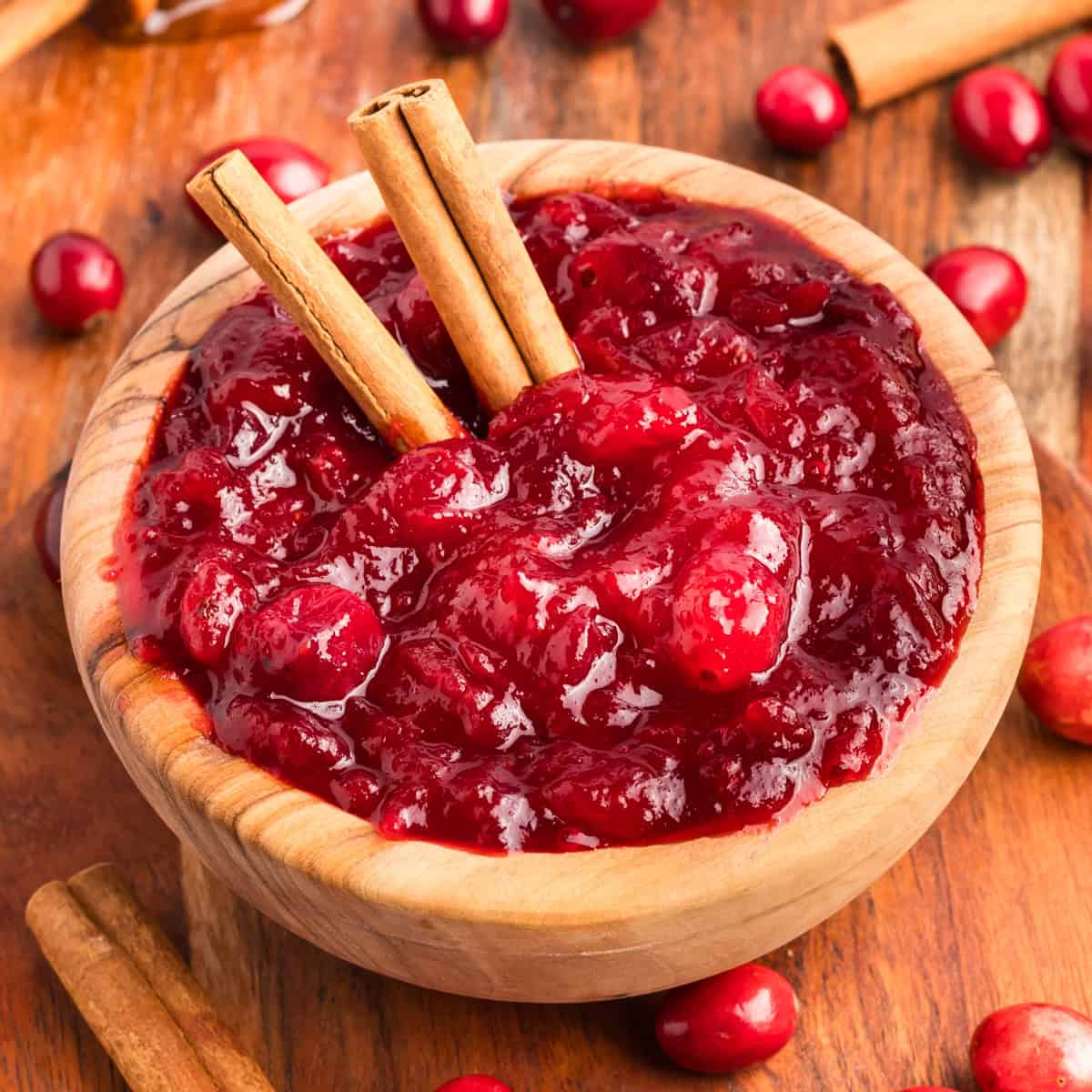 Homemade cranberry sauce in a wooden bowl with whole cranberries cinnamon sticks.