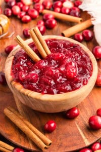 Overhead view of homemade cranberry sauce in a wooden bowl with whole cranberries cinnamon sticks.