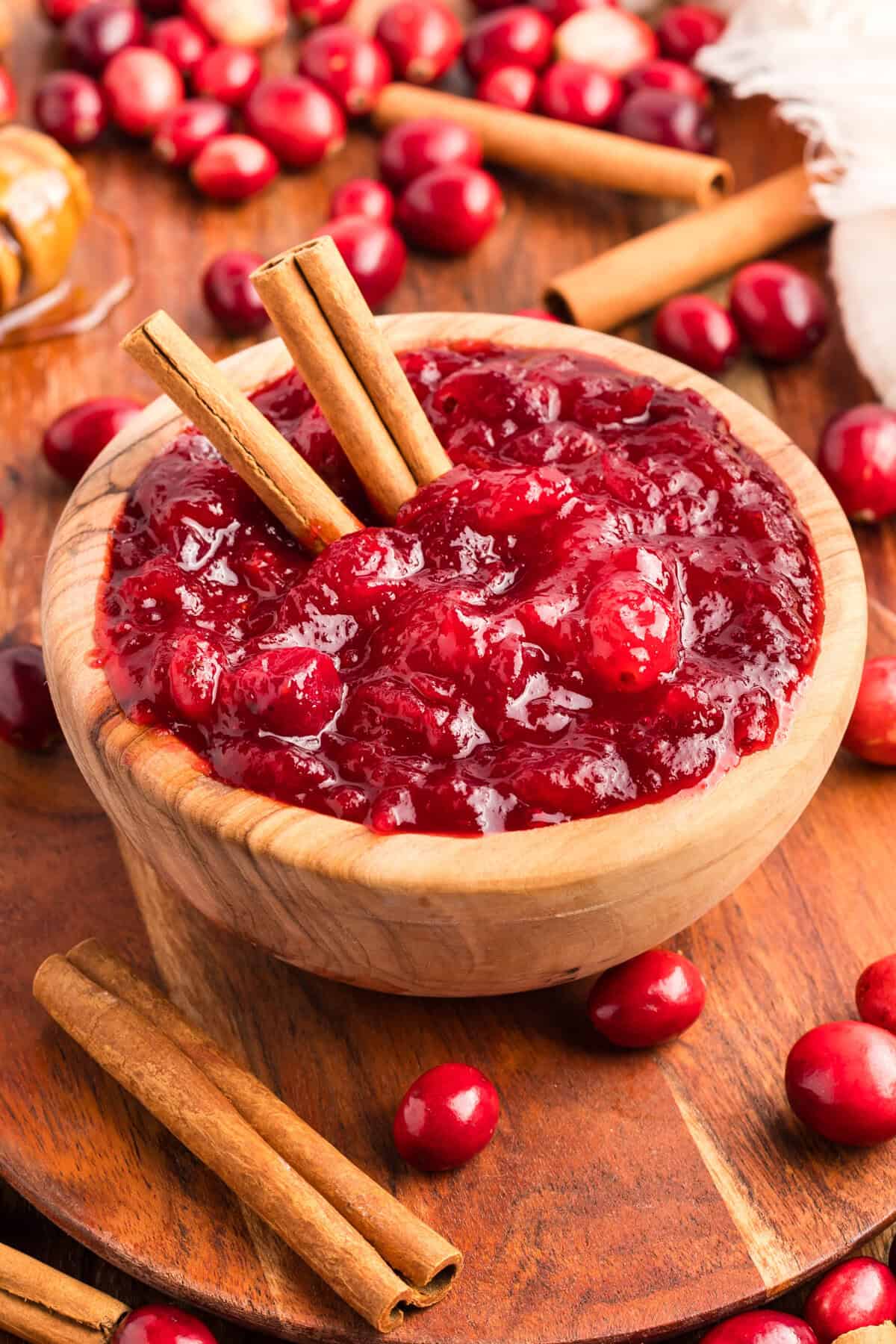Overhead view of homemade cranberry sauce in a wooden bowl with whole cranberries cinnamon sticks.