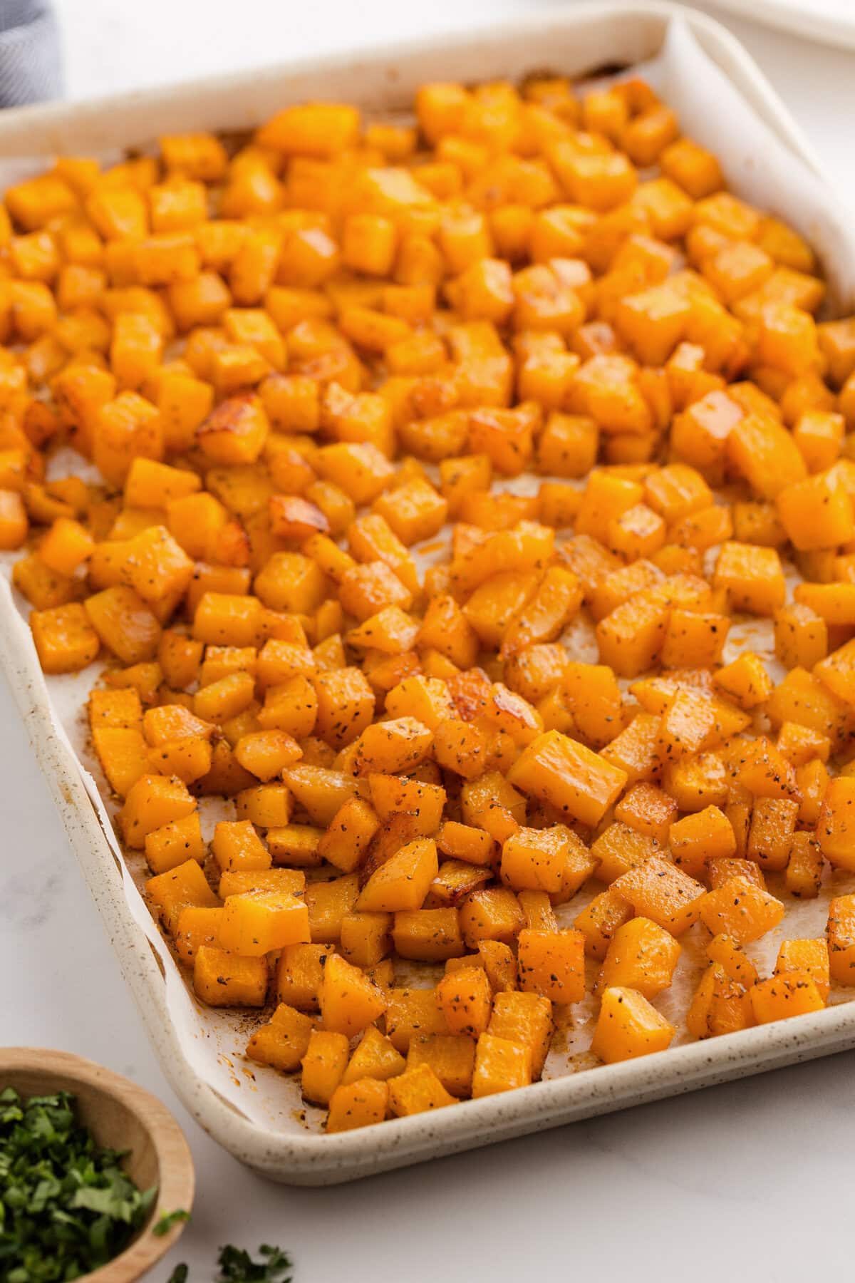 Oven roasted butternut squash spread across a lined baking sheet.