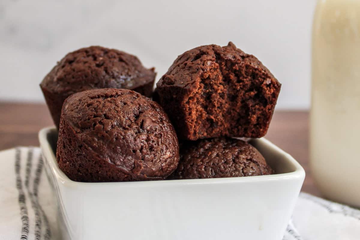 Close-up of several chocolate brownie bites in a white bowl, one brownie bite has a bite taken out of it.