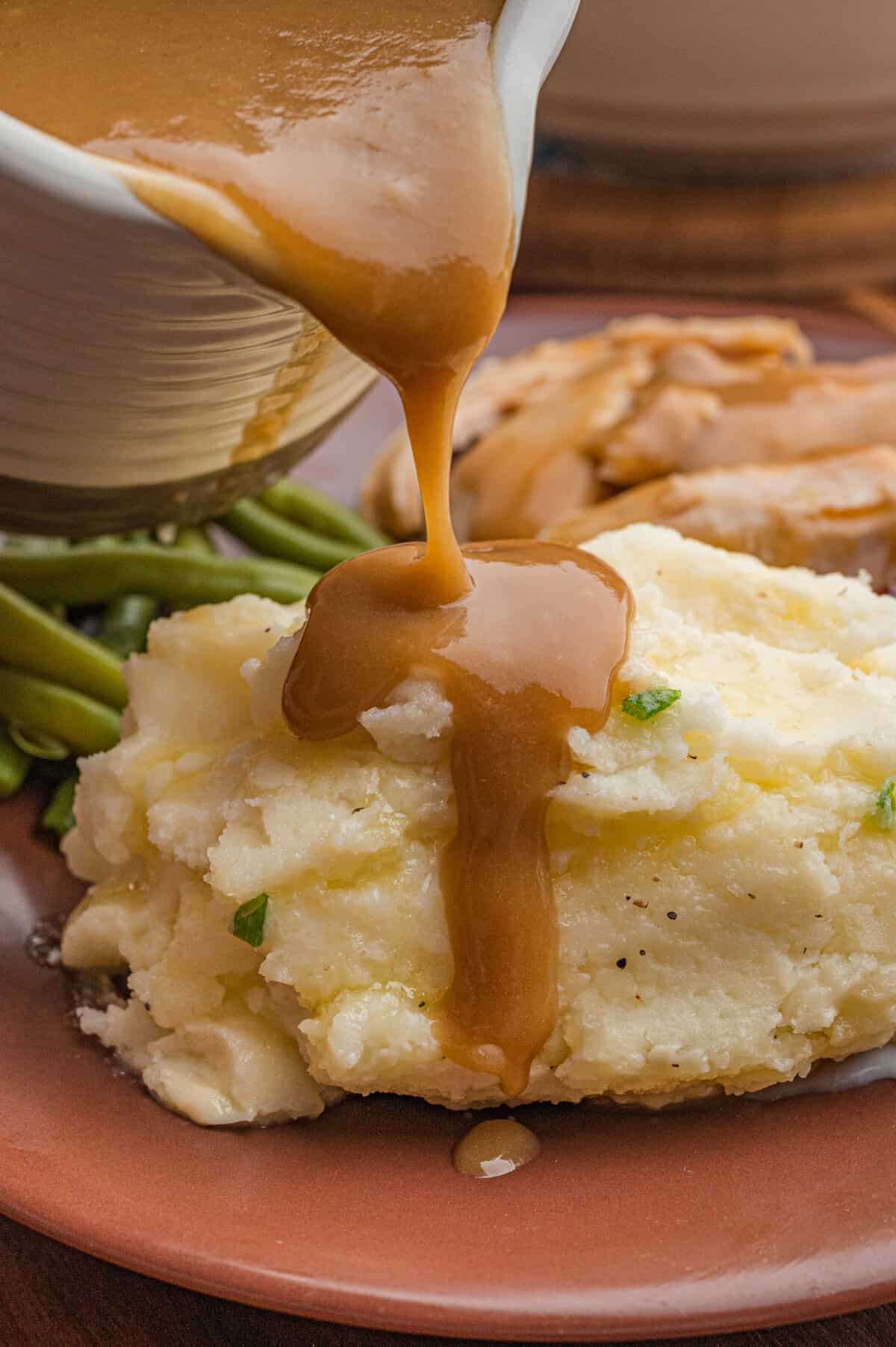 Gravy being poured over classic mashed potatoes.