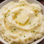 Creamy old-fashioned mashed potatoes in a bowl, topped with a square of butter, melted butter, black pepper, and chopped chives.
