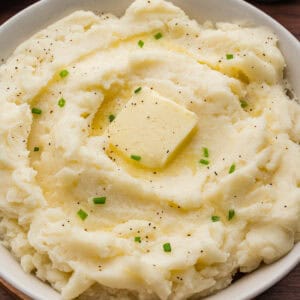 Creamy old-fashioned mashed potatoes in a bowl, topped with a square of butter, melted butter, black pepper, and chopped chives.