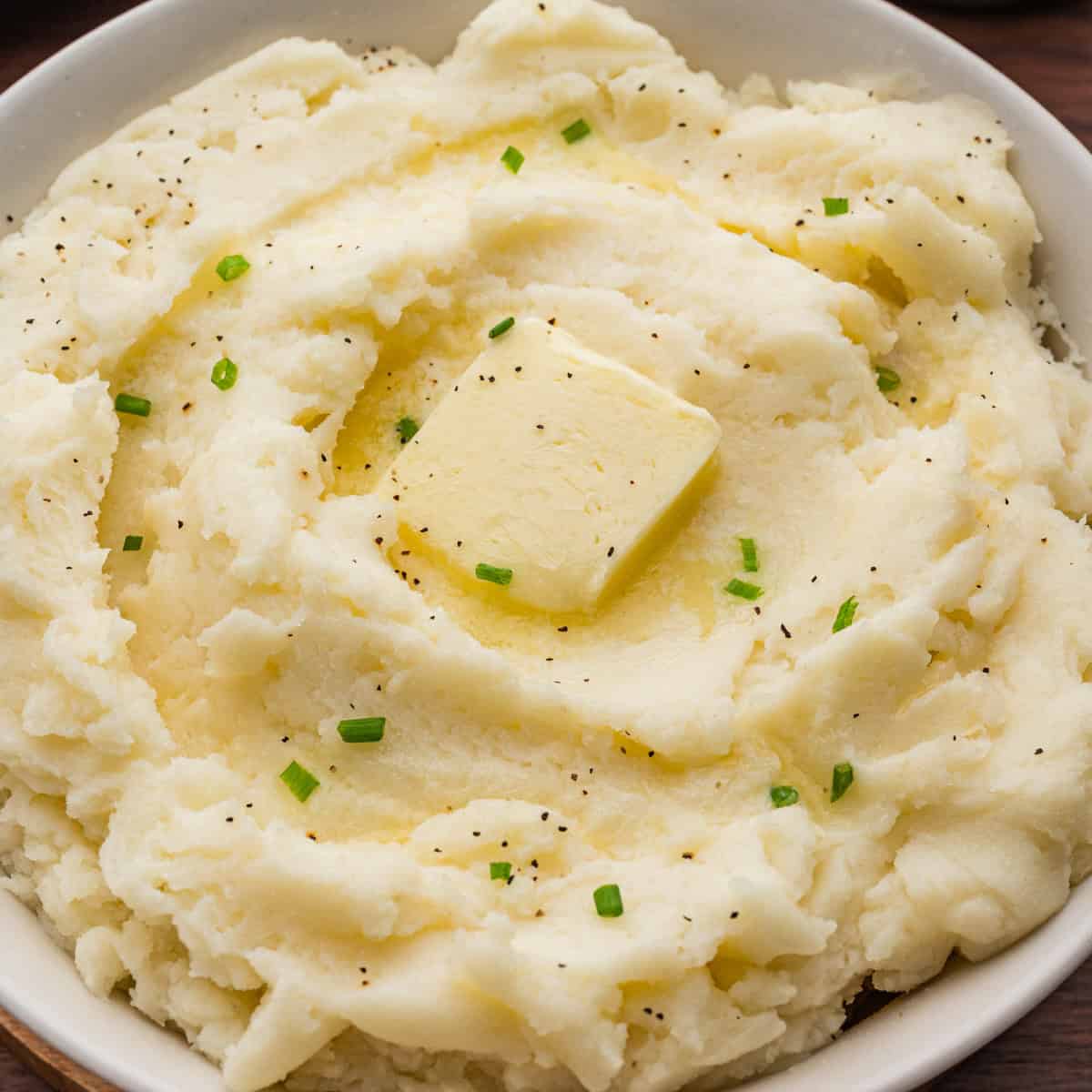 Creamy old-fashioned mashed potatoes in a bowl, topped with a square of butter, melted butter, black pepper, and chopped chives.