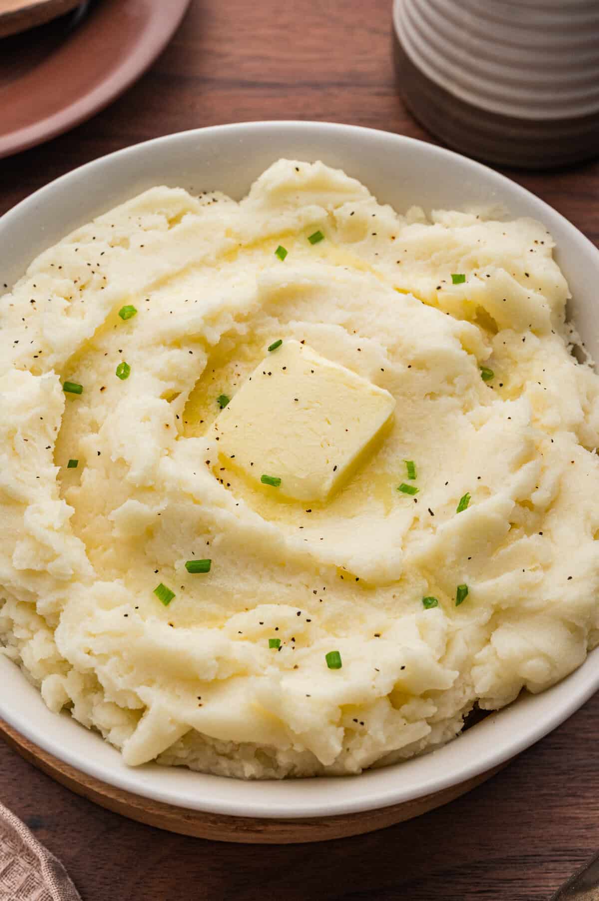 Creamy old-fashioned mashed potatoes in a bowl, topped with a square of butter, melted butter, black pepper, and chopped chives.
