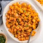 Roasted butternut squash cubes in a white serving dish with a spoon.