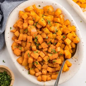 Roasted butternut squash cubes in a white serving dish with a spoon.