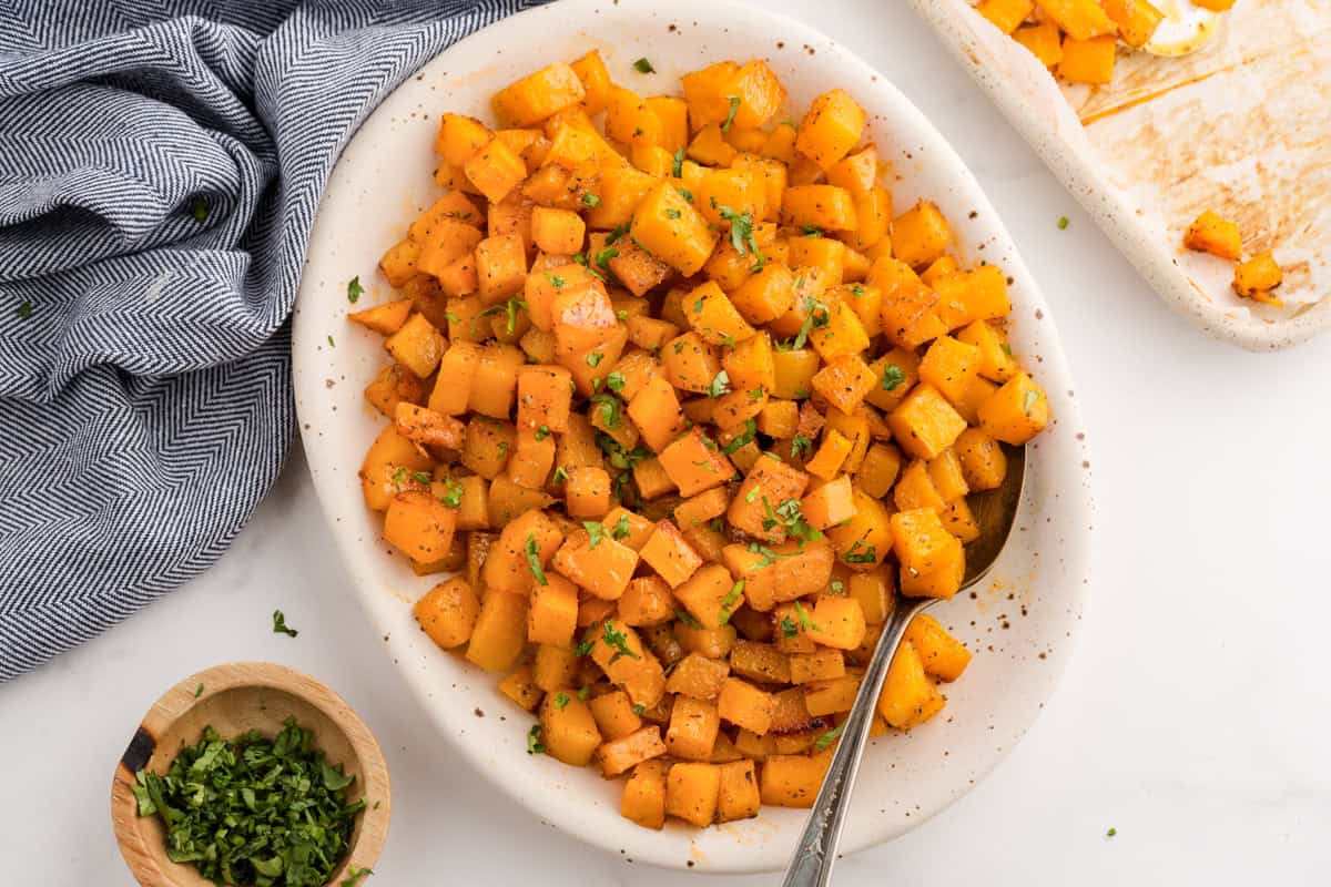 Cubed Roasted butternut squash in a white serving dish with a spoon.