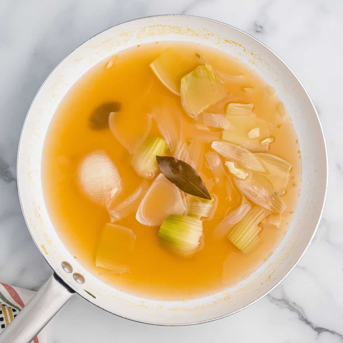 Pan of broth with onions, celery, and bay leaves.