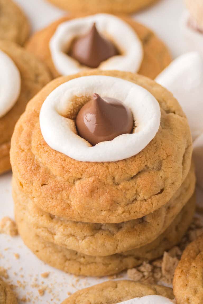 A close-up view of three stacked s'mores blossom cookies topped with gooey marshmallows and milk chocolate Hershey's kisses on top.