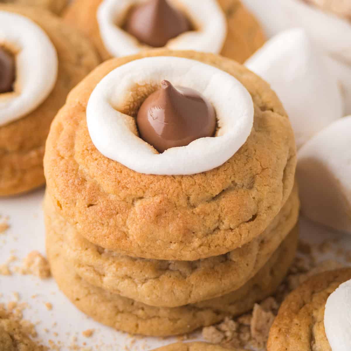 A close-up view of three stacked s'mores blossom cookies topped with gooey marshmallows and milk chocolate Hershey's kisses on top.