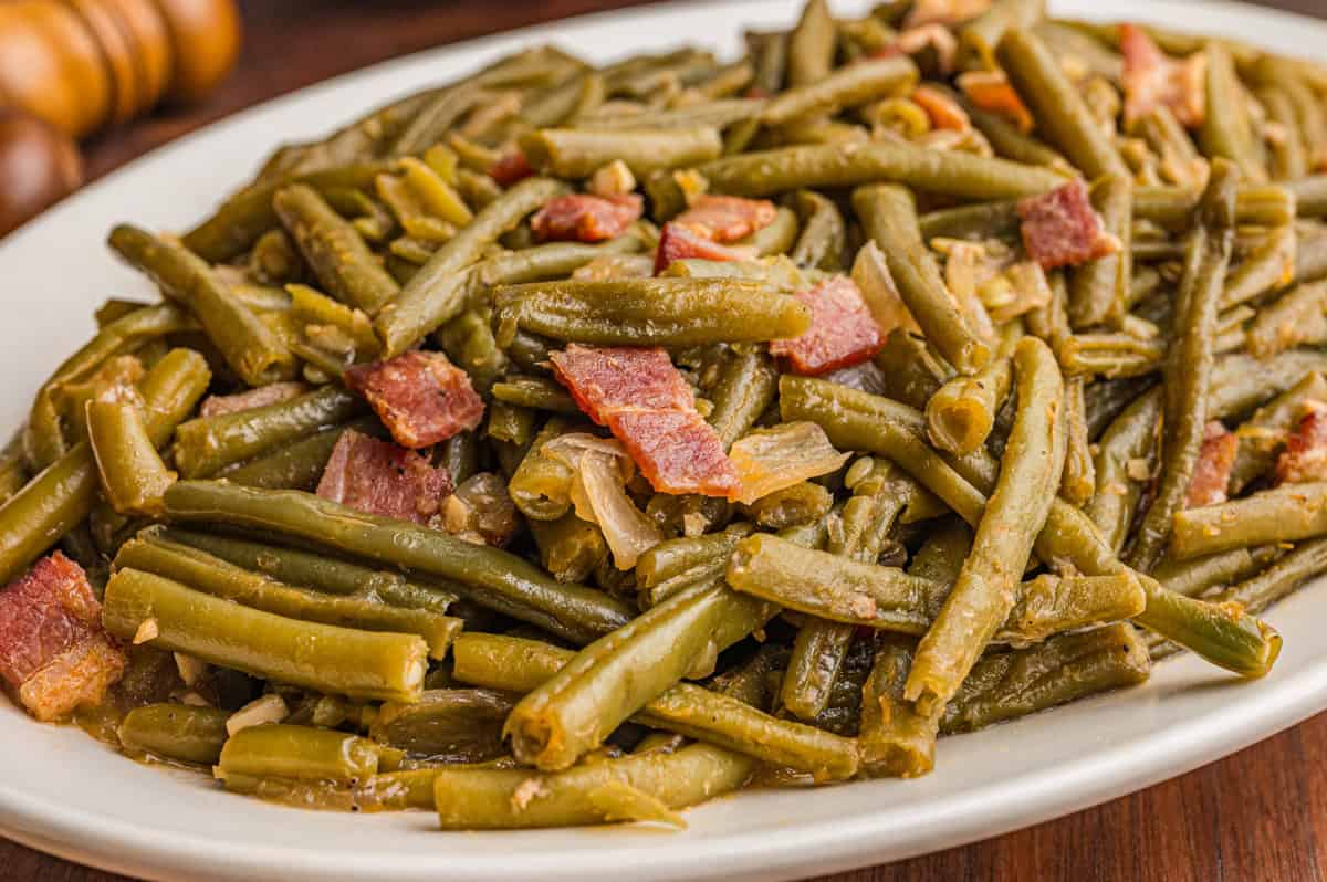 Close-up of cooked southern style green beans and bacon served on a white oval plate.