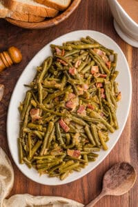 Plate of Southern green beans with bacon next to bread and gravy.