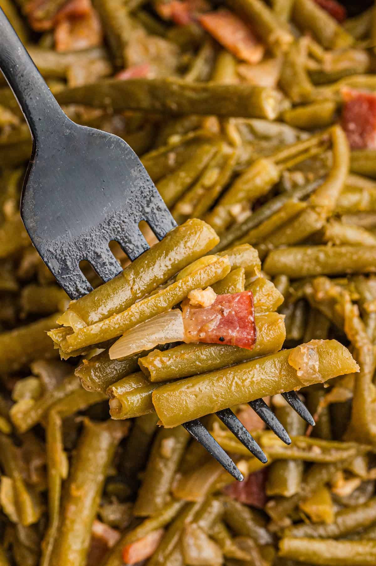 A fork picking up cooked southern string beans with bacon, onions, and garlic.