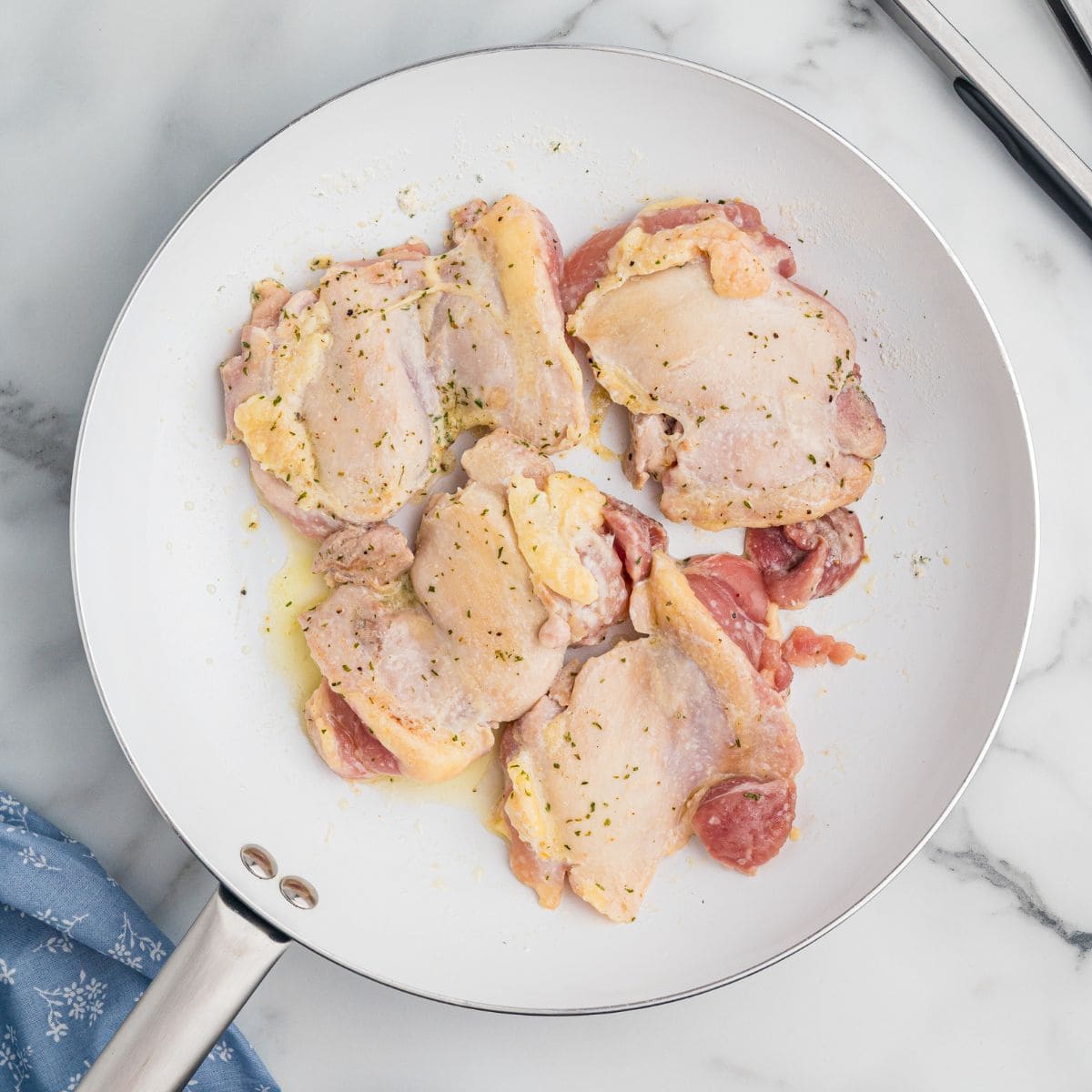 Raw chicken thighs seasoned in a white skillet.