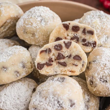 Chocolate chip snowball cookies in a bowl. The cookies are coated in powdered sugar, and a halved cookie on top shows the interior full of mini chocolate chips.