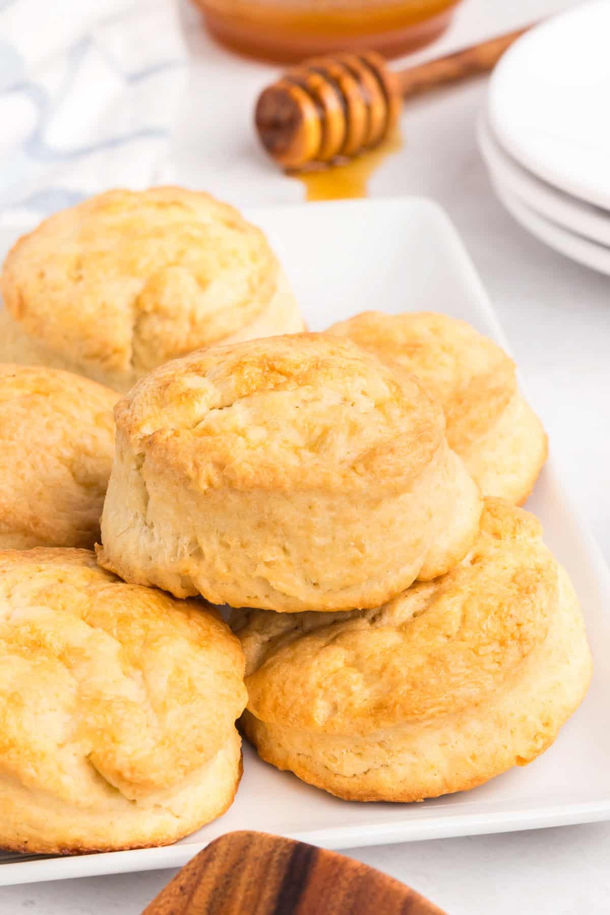 Close-up of several golden brown, fluffy biscuits stacked on a white plate, showing crisp edges and soft texture.
