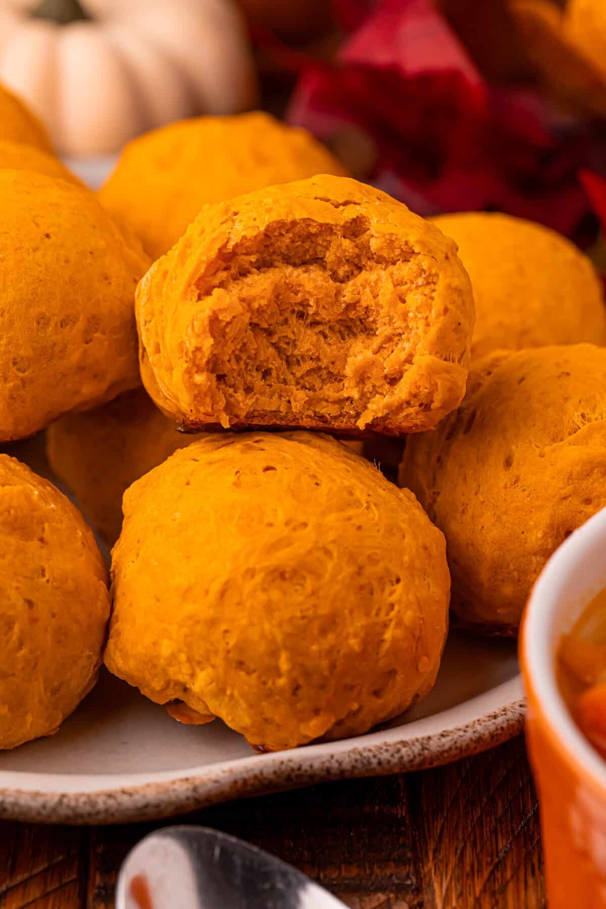 Pumpkin bread rolls are arranged on a plate, with one roll in the center showing a bite that reveals its moist, soft interior.
