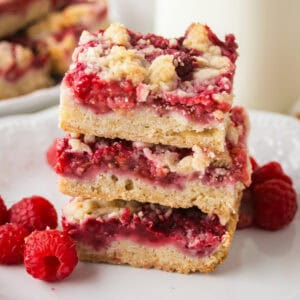 Stack of three raspberry crumble shortbread bars on a white plate with fresh raspberries.