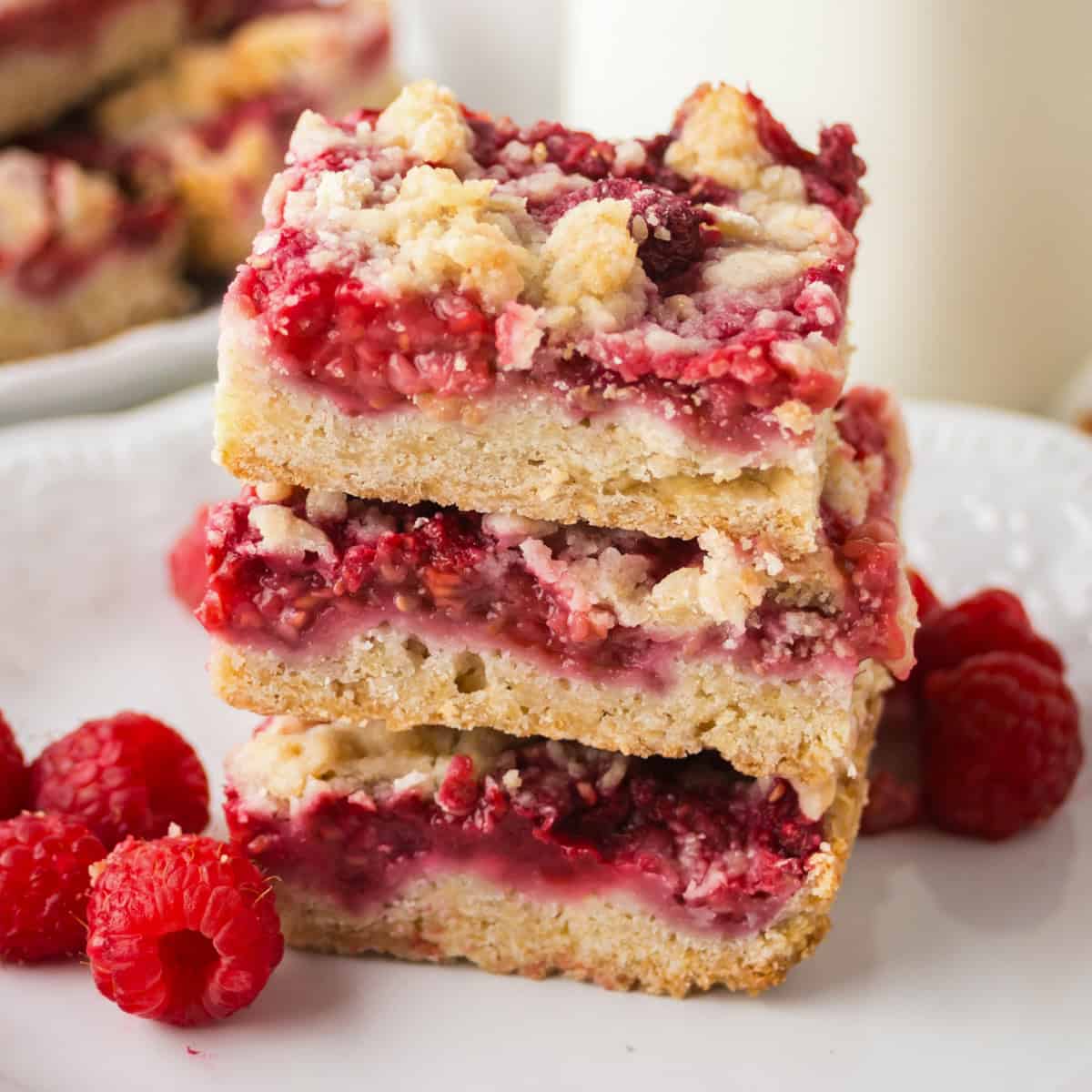 Stack of three raspberry crumble shortbread bars on a white plate with fresh raspberries.