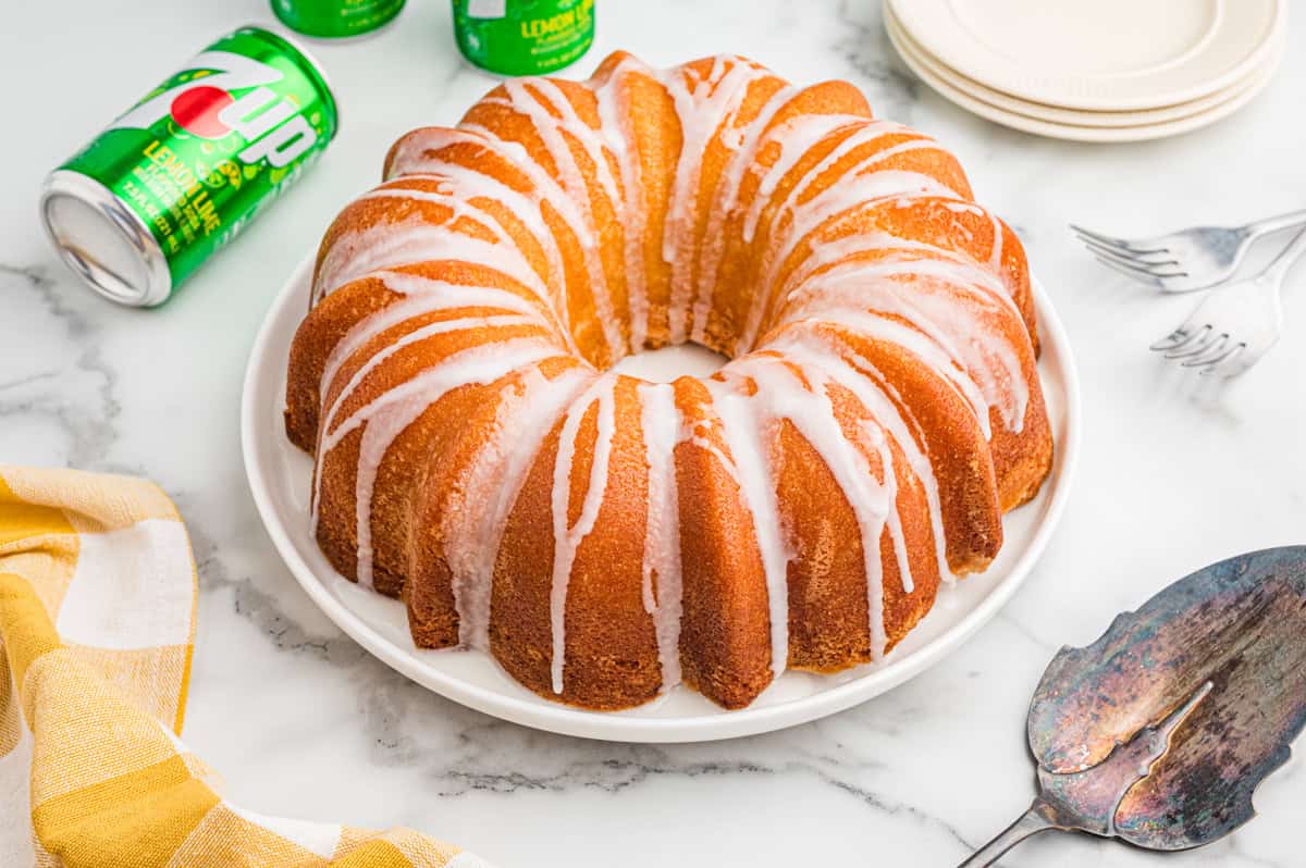 7 Up pound cake with glaze drizzled over the top and cans of 7 Up soda in the background.