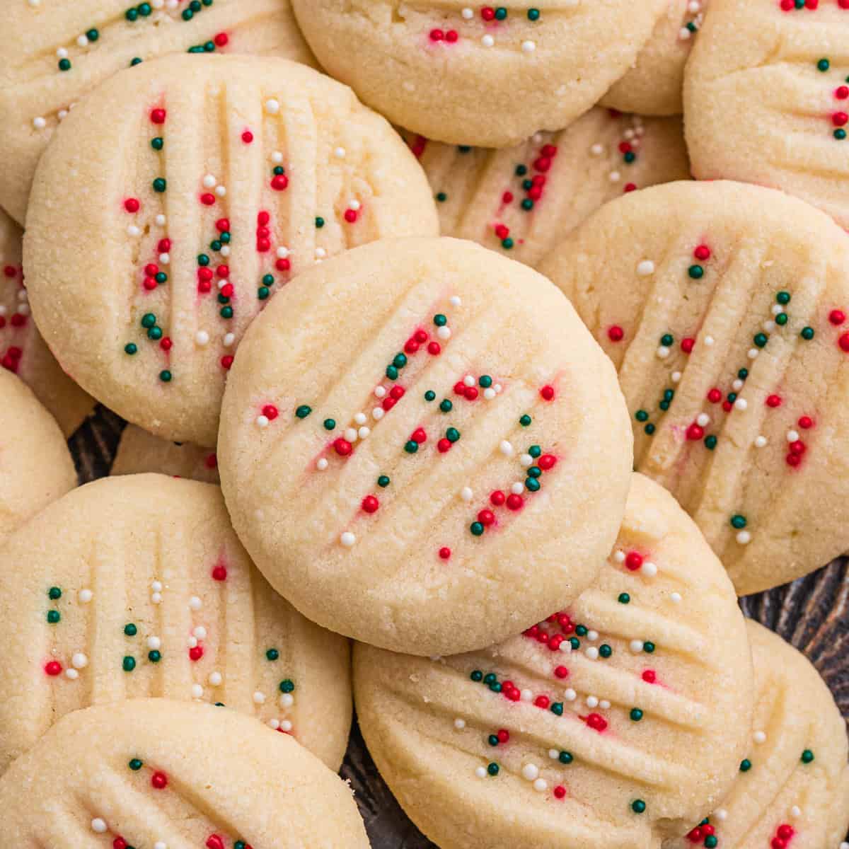 Whipped shortbread cookies with fork marks and is topped with red, green, and white nonpareil sprinkles.