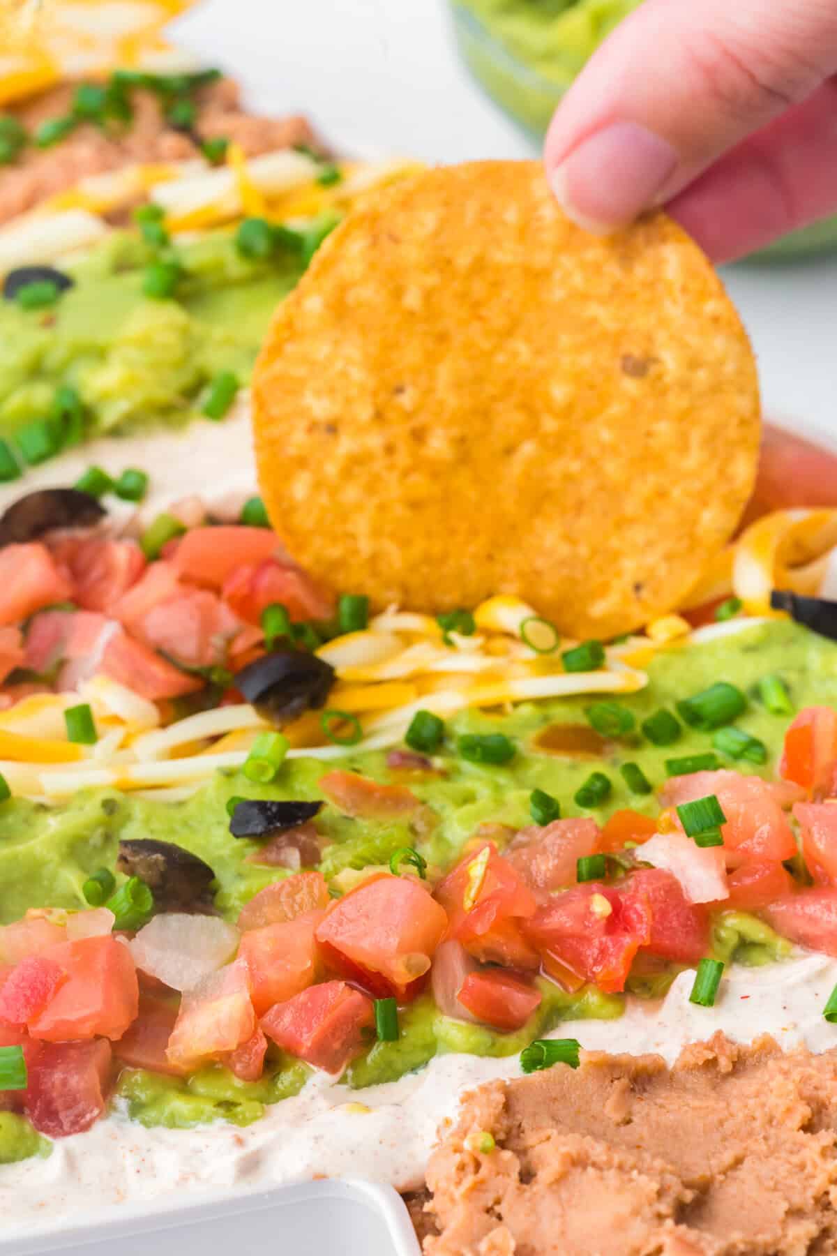 Hand dipping chip into Christmas 7 layer taco dip.