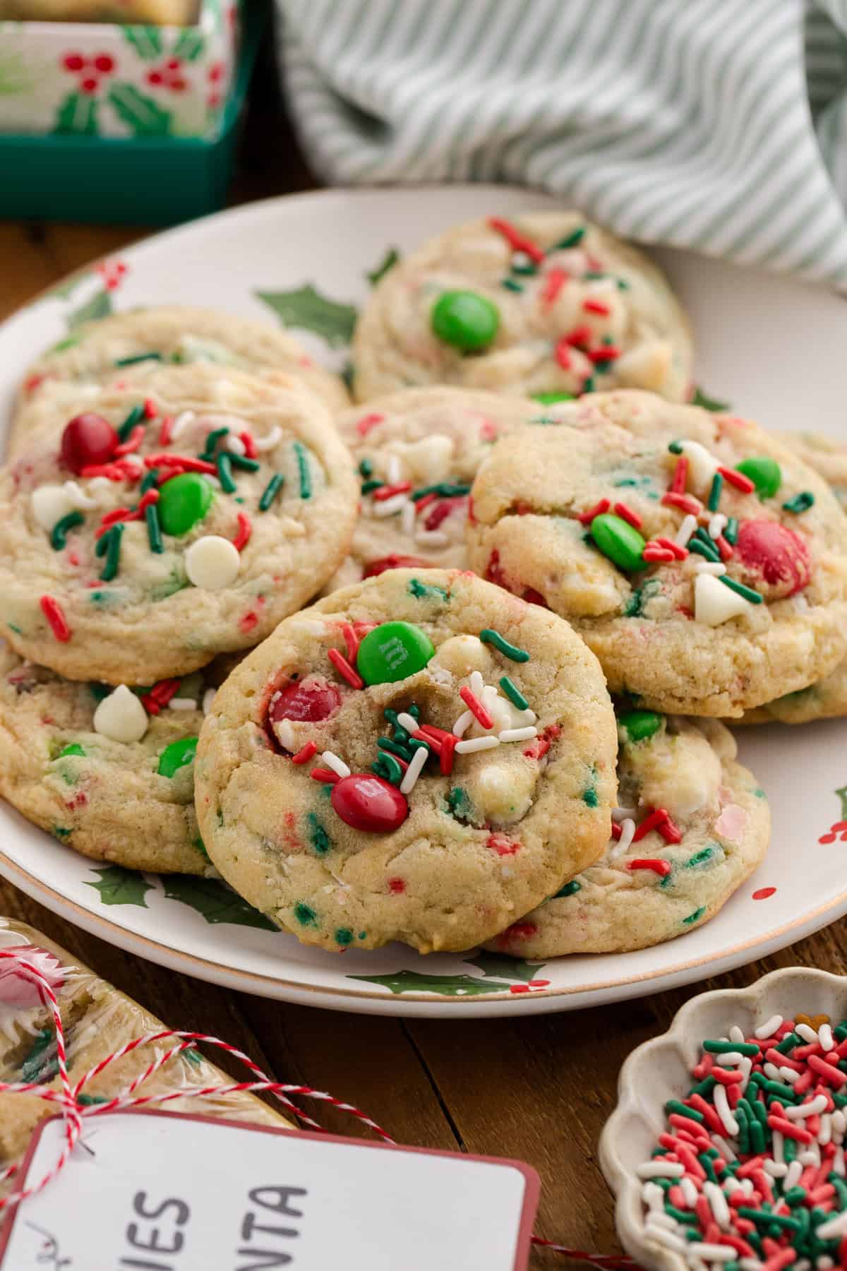 Close-up of a plate of Christmas cookies with red and green M&Ms, white chocolate chips, and colorful sprinkles.