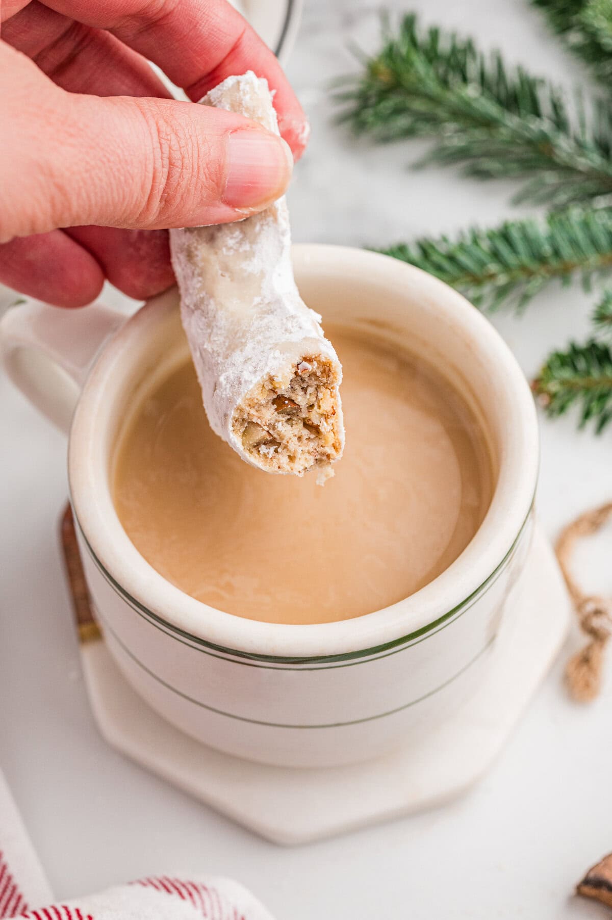 A pecan crescent cookies with powdered sugar held above a mug of coffee.