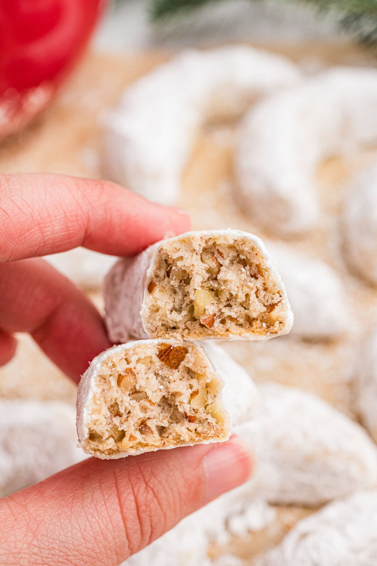 Close-up of a hand holding two halves of a pecan crescent cookie to reveal the nut-filled interior.
