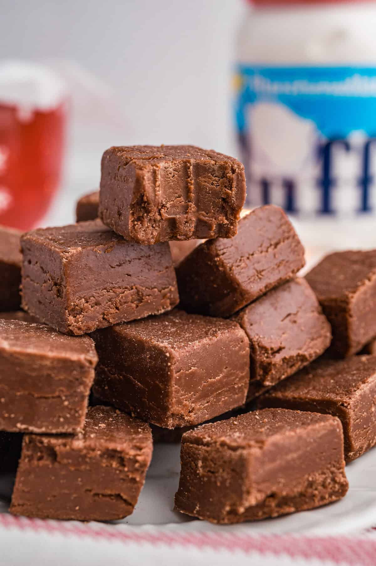 A bitten chocolate fudge made with marshmallow fluff stacked on top of other pieces with a jar of Marshmallow Fluff in the background.
