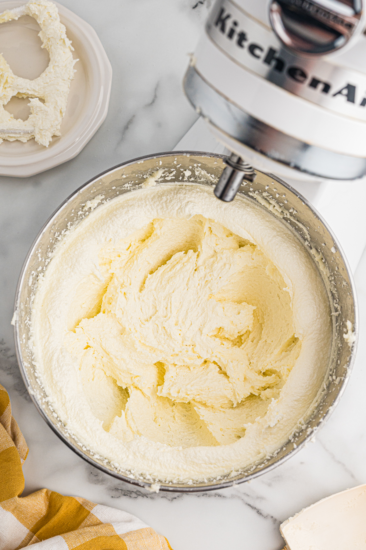 A fluffy, pale yellow mixture of creamed butter and sugar fills a metal bowl attached to a stand mixer.