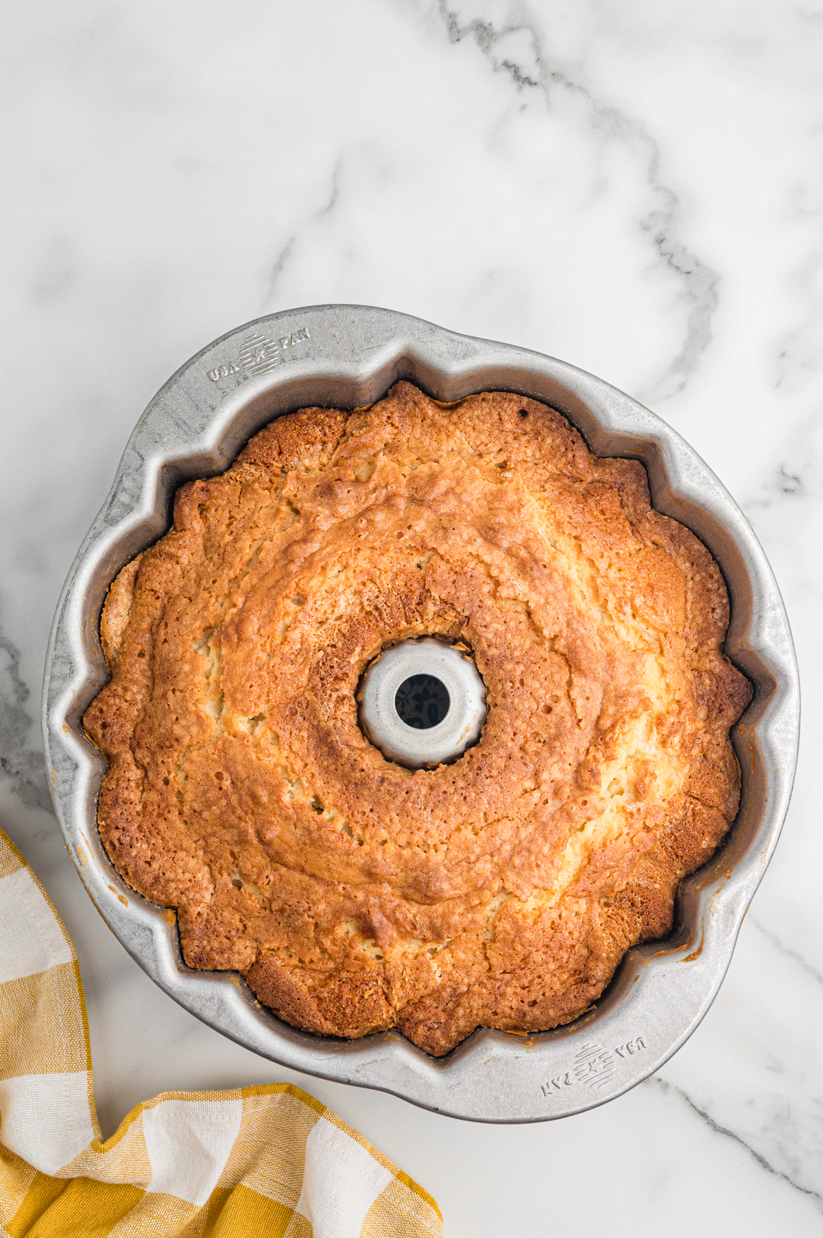 Fully baked 7 Up pound cake with a golden brown crust rests in a silver fluted Bundt pan on a marble surface. The top is domed and lightly cracked.
