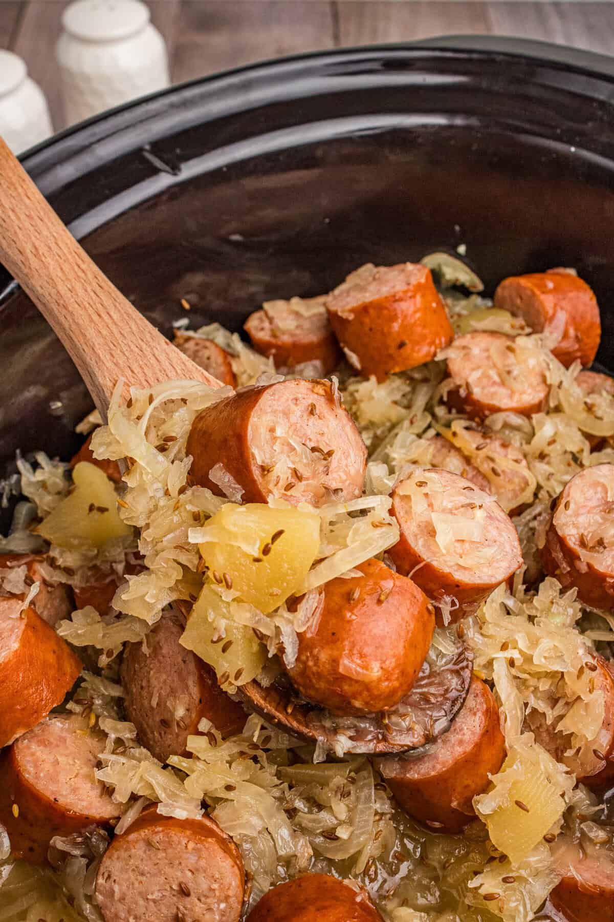 Spoon lifting kielbasa and sauerkraut from slow cooker.