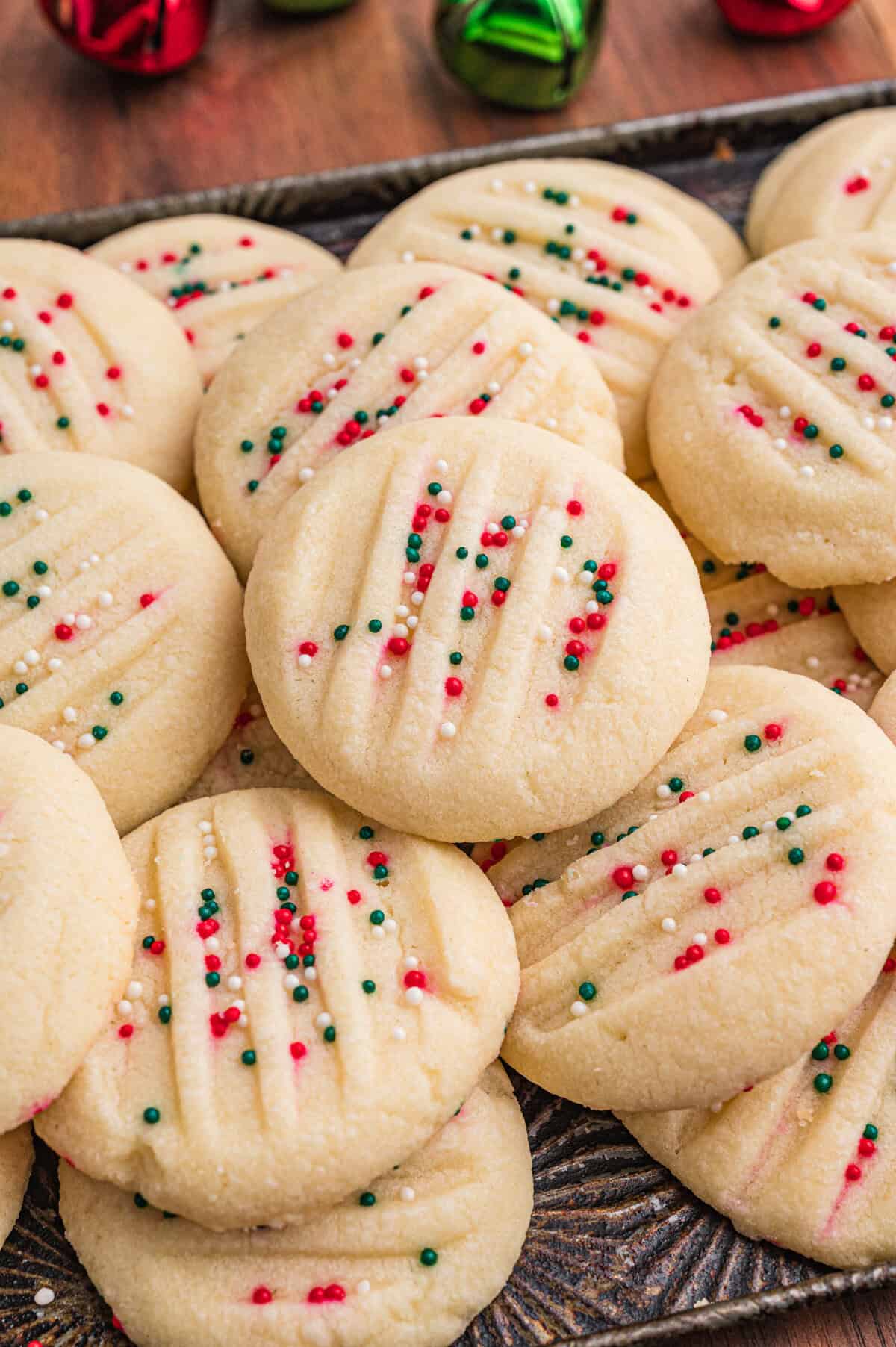 Round whipped shortbread cookies. Each cookie has fork-pressed lines and red, green, and white sprinkles.