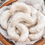 Crescent-shaped pecan cookies coated in powdered sugar, and placed in a bowl lined with parchment paper.