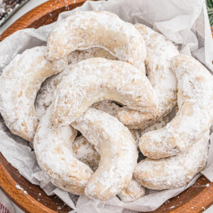 Crescent-shaped pecan cookies coated in powdered sugar, and placed in a bowl lined with parchment paper.