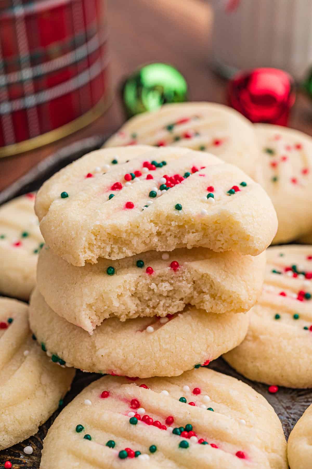 Stack of shortbread cookies with red, green, and white sprinkles; top two cookies have a bite taken out, showing a soft, crumbly texture.