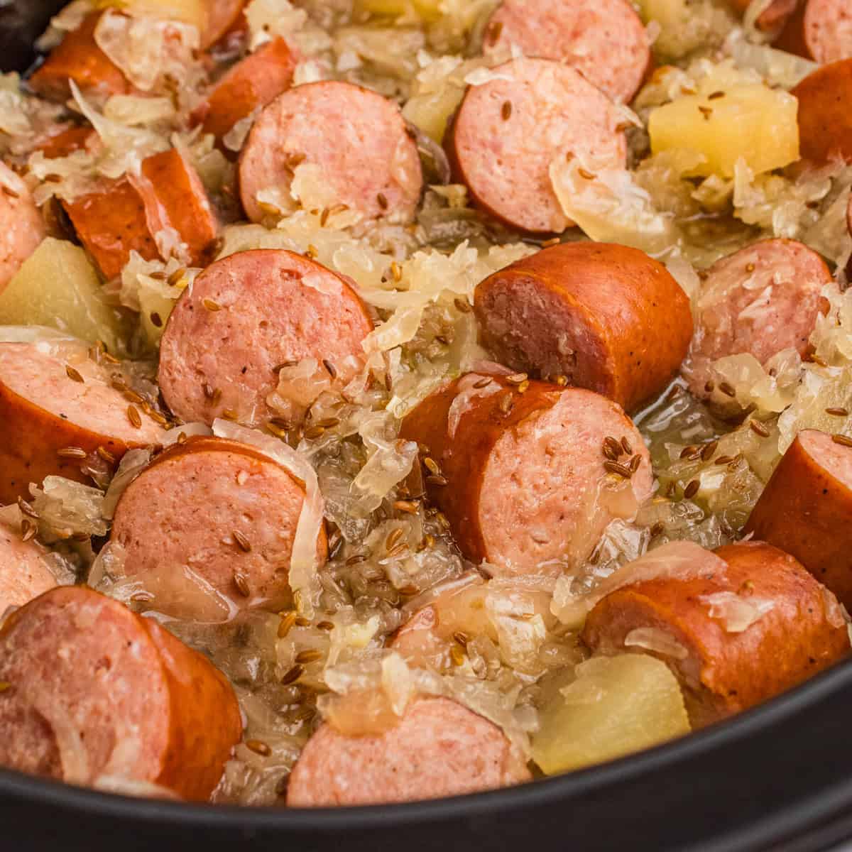 Kielbasa with sauerkraut, caraway seeds, and apple chunks in a crock pot.