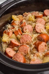 Kielbasa with sauerkraut, caraway seeds, and apple chunks in a crock pot.