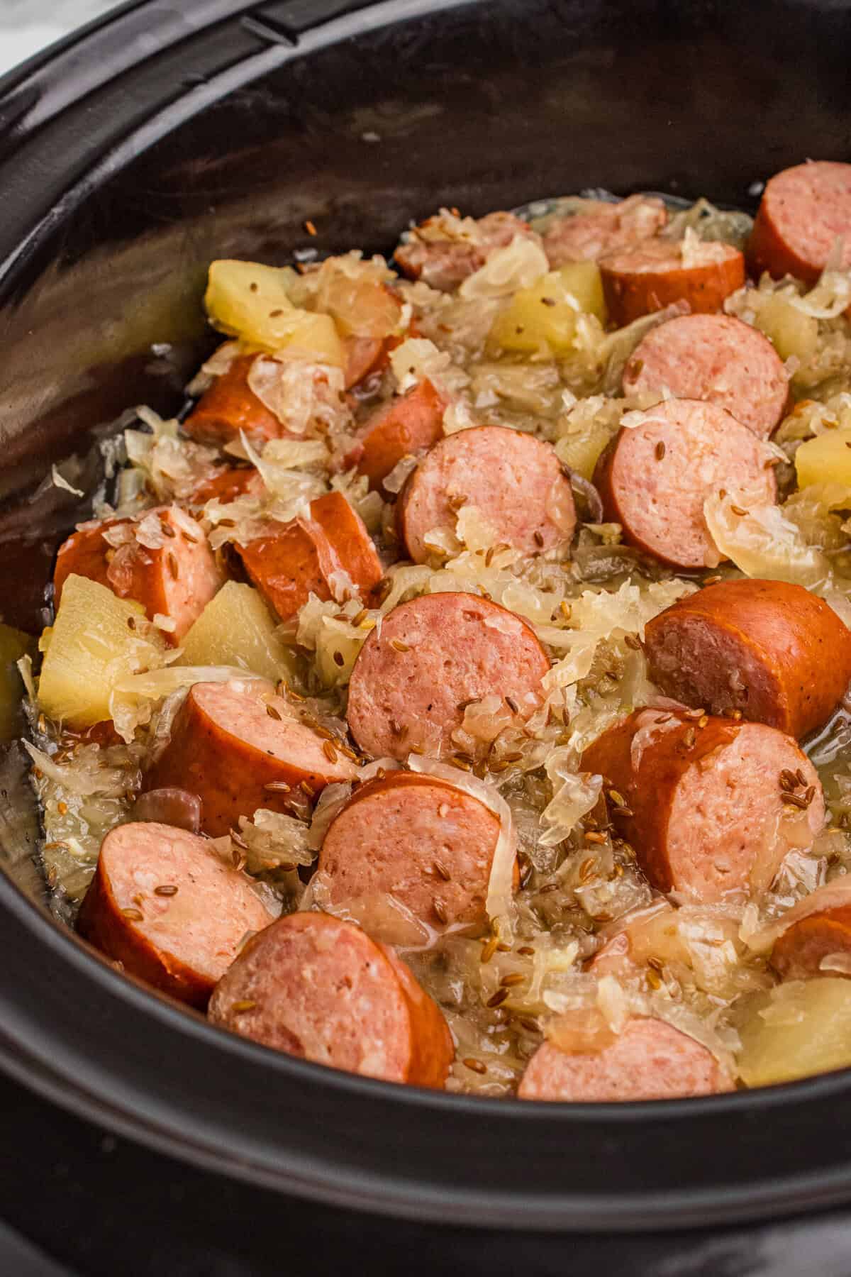 Kielbasa with sauerkraut, caraway seeds, and apple chunks in a crock pot.