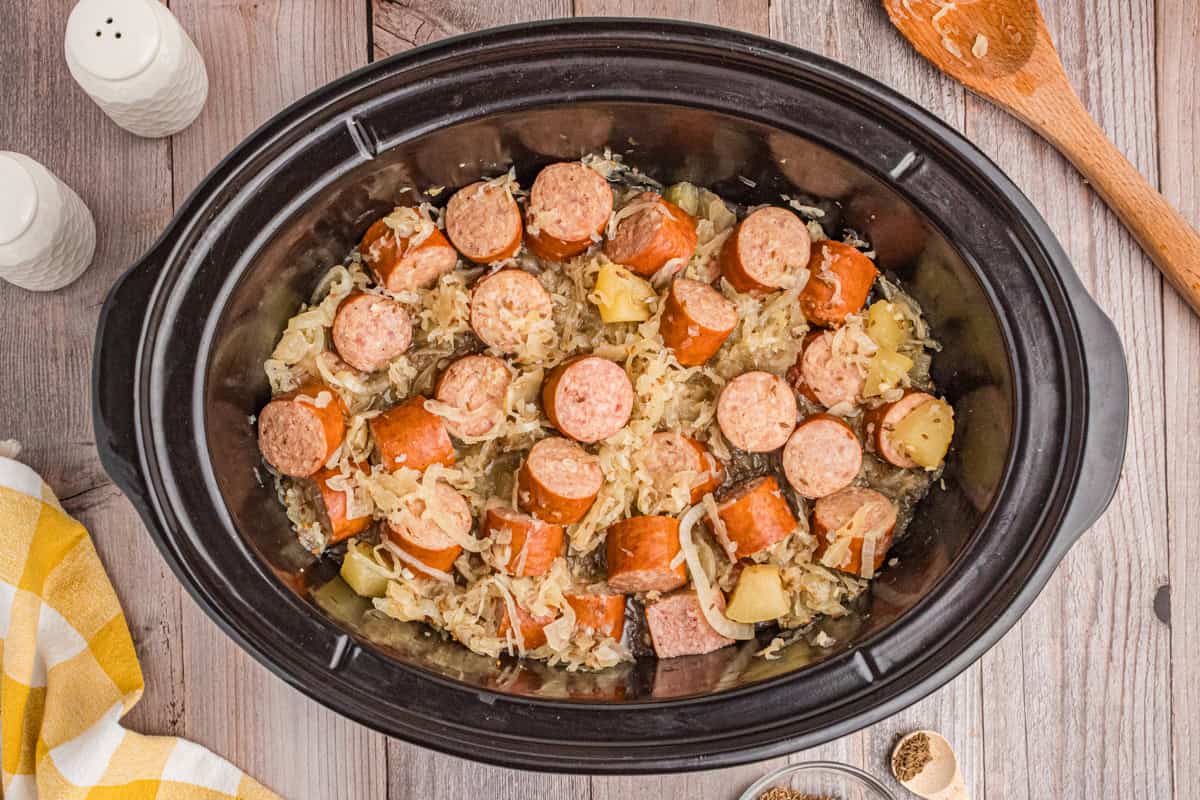 Sliced kielbasa with sauerkraut and apples in a slow cooker.
